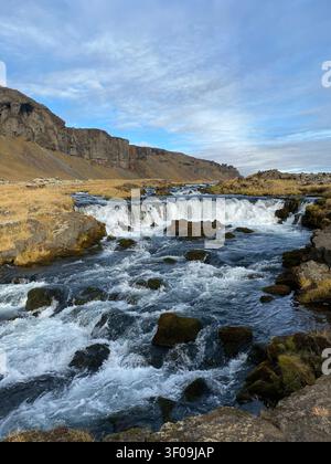 Ein malerischer Blick auf einen kleinen, kaskadierenden Wasserfall, der über vulkanische Felsen in der zerklüfteten, herbstlichen Wildnis Islands fließt Stockfoto