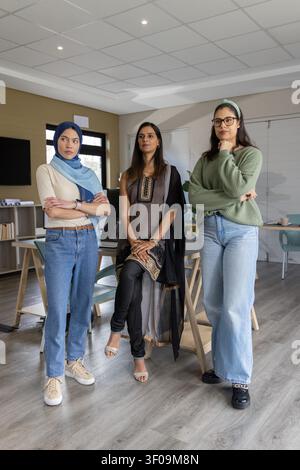 Verschiedene weibliche Kollegen stehen im Besprechungsraum, tragen Hijab und Tunika und halten einen Laptop. Büro, Arbeitsbereich, Zusammenarbeit, Teamarbeit, professionell, modern, minimalistisch Stockfoto