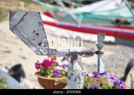 Eine Nahaufnahme eines alten, verwitterten Metall-Windrohrs und Anemometers mit abblätternder weißer Farbe, vor einem wunderschön unscharfen Hintergrund aus Farben Stockfoto