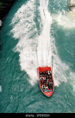 Eine Luftaufnahme zeigt das rote Boot „Shotover Jet“ mit Passagieren, das den teal-farbenen Shotover River navigiert und einen weißen Kielwellen erzeugt. Gefilmt auf 35mm Ul Stockfoto