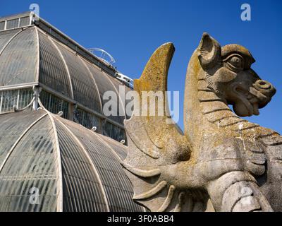 Die Bestien der Königin vor dem berühmten PAL House der Royal Botanic Gardens in Kew, England. Dieses revolutionäre viktorianische Gebäude wurde 1848 erbaut und war das erste Gewächshaus in diesem Maßstab sowie das erste große strukturelle Material, das Schmiedeeisen verwendet wurde. The Queen's Beasts – eine Reihe von heraldischen Statuen, die die Abstammung von Königin Elizabeth II darstellen – bewachen jetzt das Palmenhaus. Es handelt sich um Repliken aus Portland Stone der Statuen, die ursprünglich von dem Bildhauer James Woodford für die Krönung von Königin Elizabeth II. Im Jahr 1953 in der Westminster Abbey entworfen wurden. Der weltberühmte Kew Botanic Gard Stockfoto