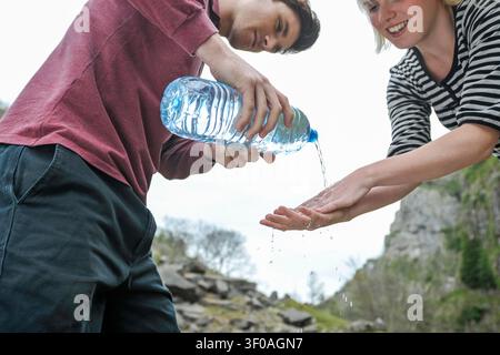 junger Mann wäscht die Hände einer Frau draußen, indem er Wasser aus einer Plastikflasche gießt Stockfoto