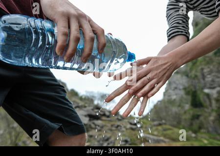 Nahaufnahme eines jungen Mannes, der die Hände einer Frau wäscht, indem er Wasser aus einer Plastikflasche gießt, auf dem Land Stockfoto