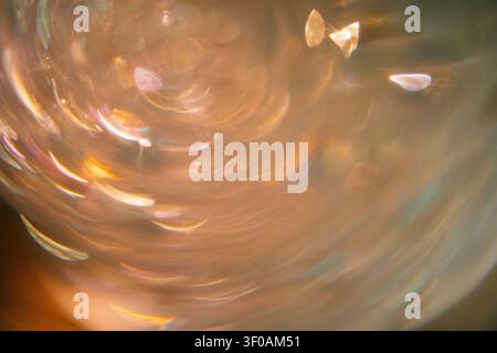 Nahaufnahme von wirbelndem Glas mit farbenfrohen Reflexionen und Lichtmustern, das einen abstrakten visuellen Effekt mit einem weich fokussierten Hintergrund erzeugt Stockfoto