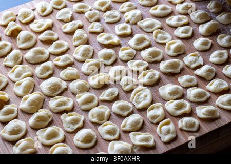 Dutzende von rohen handgemachten Orecchiette-Pasta in Reihen auf einem bemehlten Holzbrett angeordnet, Blick von oben, traditionelles apulisches Nudelmachen Stockfoto