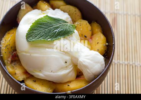 Gourmet-Sommersalat mit cremigem Burrata-Käse, gepaart mit frischen geschnittenen Nektarinen und Basilikum, serviert auf einem Teller. Stockfoto