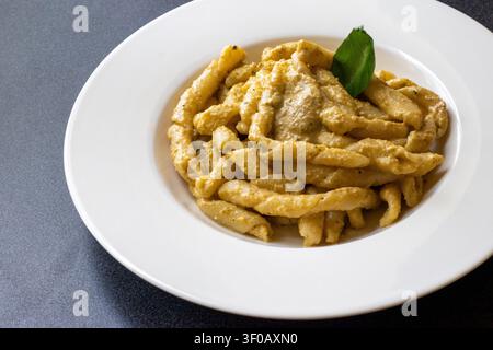 Busiate-Pasta mit cremigem Trapanese-Pesto und einem Basilikumblatt auf einem weißen Teller mit breitem Rand auf einer dunkelgrauen gesprenkelten Oberfläche, sizilianische Küche Stockfoto