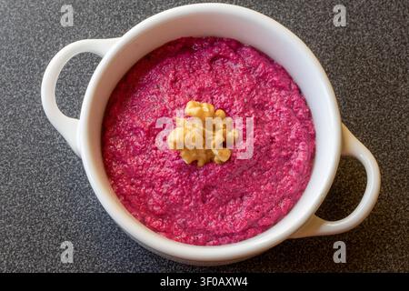 Überkopf-Flachlage-Aufnahme einer runden weißen Schüssel, gefüllt mit auffälliger rosa Rote-Bete-Cremesauce und garniert mit einer Walnuss. Stockfoto