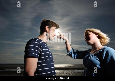Junge Frau zeigt mit dem Finger auf den Kopf eines jungen Mannes, während die Sonne am Verbindungspunkt aufflammt Stockfoto