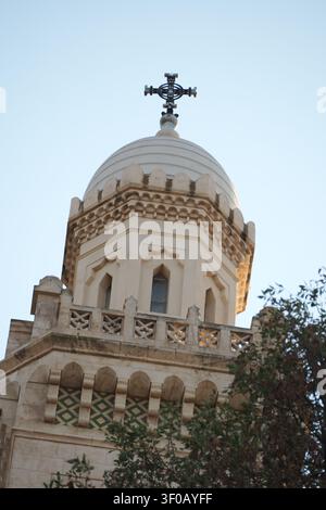 Eine klare niedrig angelegte Aufnahme, die sich auf die majestätische weiße Kuppel und die kunstvollen Fenster der Basilika Notre-Dame d'Afrique konzentriert, die mit einem christlichen Kreuz gekrönt ist und Stockfoto