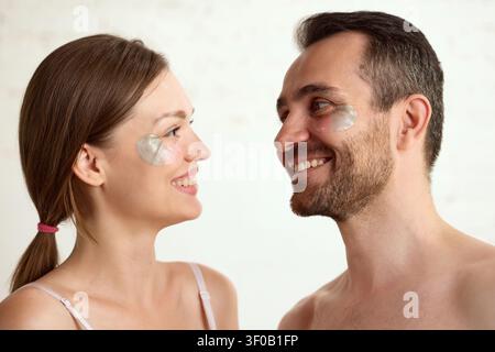 Lächelndes reifes Ehepaar unter Augenpflaster während der Hautpflegeroutine. Stockfoto