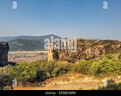 Kalambaka, Griechenland – 24. Juli 2024: Meteora-Klosterensemble. Weit unten die Stadtlandschaft von Kalambaka. Weite Landschaft mit Gebirgszug am Horizont. Stockfoto