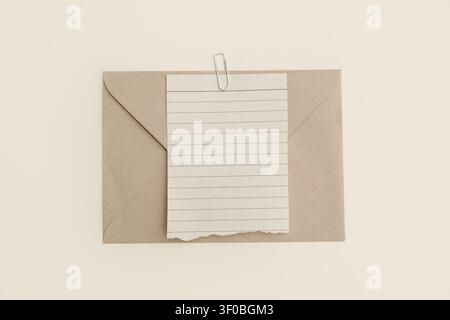 Vintage-Kraft-Umschlag, zerrissenes liniertes Notizpapier, weißer Büroklammer. Neutraler beiger Tischhintergrund. Minimales Schreibwaren-Mockup für Brief, Nachricht Stockfoto