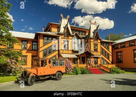 Dalen, Norwegen - 16.06.2026: Klassischer antiker Bus vor dem prunkvollen Dalen Hotel im Drachenstil mit üppigem Grün und Sommersonne Stockfoto