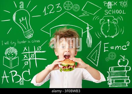 Überraschtes Kind im Unterricht. Lustiges Kind vor grüner Kreidetafel. Zurück zur Schule und Bildungsbegriff Stockfoto