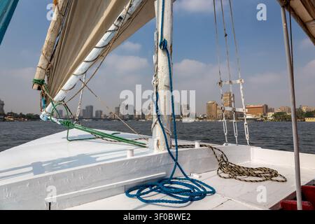 Traditionelles Felucca-Holzrumpfsegelboot auf dem Nil, Blick auf das Deck mit natürlichem Baumwollsegel, Seilen und Takelage, Giza-Landschaft mit Nasser-Residenz. Stockfoto