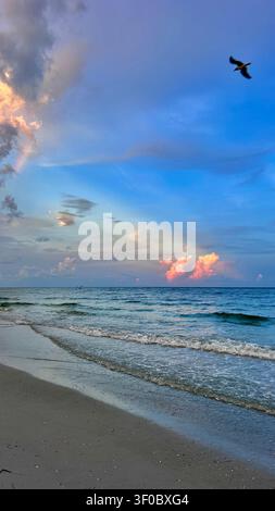 Ein atemberaubender Sonnenaufgang über dem Meer mit sanftem goldenem und orangefarbenem Licht, das den Himmel erhellt und sich über sanfte Wellen spiegelt. Friedlicher Sandstrand Stockfoto