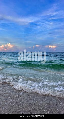 Ein atemberaubender Sonnenaufgang über dem Meer mit sanftem goldenem und orangefarbenem Licht, das den Himmel erhellt und sich über sanfte Wellen spiegelt. Friedlicher Sandstrand Stockfoto