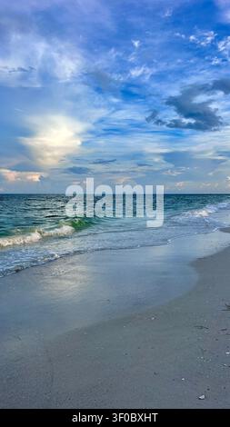 Ein atemberaubender Sonnenaufgang über dem Meer mit sanftem goldenem und orangefarbenem Licht, das den Himmel erhellt und sich über sanfte Wellen spiegelt. Friedlicher Sandstrand Stockfoto