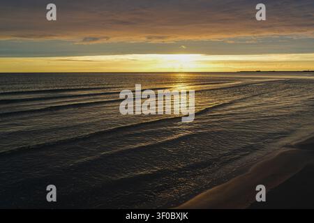 Goldener Sonnenuntergang über der Ostsee mit ruhigen Wellen, leuchtendem Horizont und sandigem Strand, der eine friedliche Küstenlandschaft am Abend schafft Stockfoto
