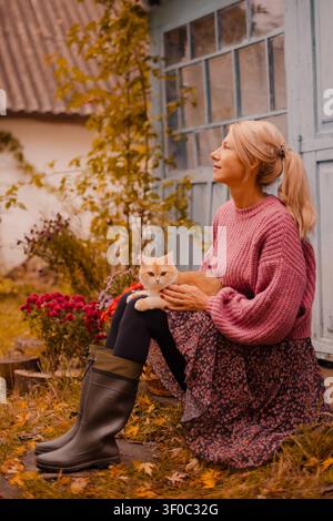 Reife Frau, die in einem Herbstgarten Ingwer-Kurzhaarkatze hält Stockfoto