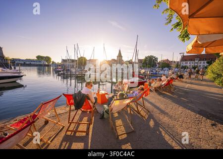 Menschen entspannen auf Sonnenliegen an der Hafenpromenade bei Sonnenuntergang, Lindauer Insel, Bodenseekreis, Deutschland Stockfoto