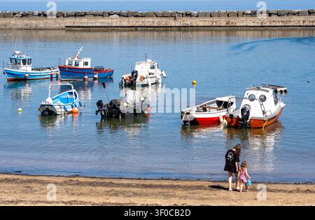 Mutter und junge Tochter genießen einen sonnigen Tag am Strand von Staithes Harbour, teilen einen entspannten Küstenmoment in diesem historischen Fischerdorf in North Yorkshire Stockfoto