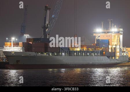 Das Containerschiff Henneke Rambow (IMO 9354430) legte in einem beleuchteten Hafenterminal unter Kränen bei Nacht während des Ladebetriebs an. Seitenansicht. Stockfoto