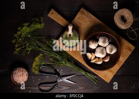 Frischer Dill, ganze Knoblauchzwiebeln, Knoblauchzehen, rosafarbenes himalaya-Salz und getrocknete Dillflocken mit wichtigen Zutaten für die Hausmannskost im Dunkeln Stockfoto
