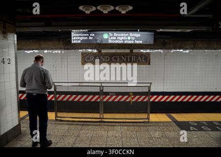 New York City, USA - 7. Juli 2026: Ein Fahrgast wartet auf dem Bahnsteig im U-Bahnhof Grand Central in New York City. Richtungsschilder für die Downtown Stockfoto