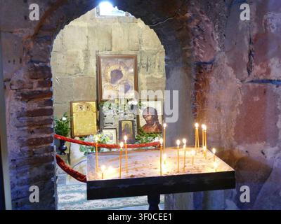 GEORGIEN, KAUKASUS - 27. APRIL 2024 - Beleuchtete Kerzen erhellen orthodoxe Ikonen und Steinmauern in einer alten Kirche in Georgien, die religiöse darstellt Stockfoto