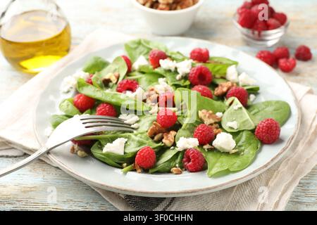 Appetitlicher Salat mit Spinat, Käse, Walnüssen und Himbeeren, serviert auf altem Holztisch, Nahaufnahme Stockfoto