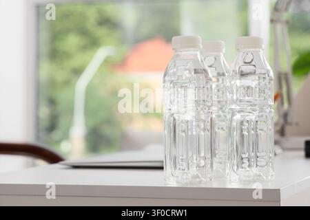 Drei Wasserflaschen aus Kunststoff auf weißem Tisch im Innenbereich Stockfoto