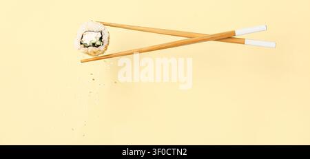 Sushi-Brötchen, gehalten von Stäbchen mit herabfallenden Sesamsamen Stockfoto