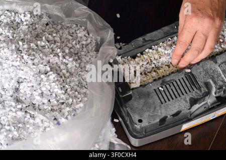Nahaufnahme aus hohem Winkel, die eine Hand zeigt, die verklemmtes Geschreddertes Papier von den Schredderklingen neben einem Abfallbeutel entfernt Stockfoto