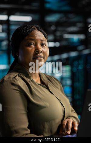 Frau in Servereinrichtung arbeitet mit Notebook-Computer, um Backend-Betriebsinfrastruktursysteme zu beheben. Stockfoto