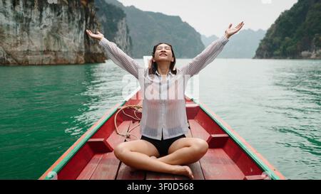 Asiatische Frau fühlt Freiheit und Glück auf einem traditionellen Boot im Khao-Sok-See Stockfoto