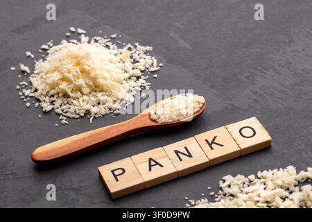 Holzlöffel mit Panko-Brotkrümeln auf einem dunklen Hintergrund, begleitet von Holzbriefen, die "PANKO" buchstabieren. Stockfoto
