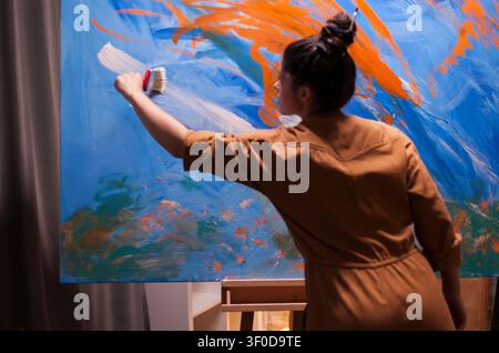Frau malt auf einer großen weißen Leinwand in einem Kunststudio und erschafft zeitgenössische Kunstwerke mit Kreativität, Handwerk und Fokus auf bildende Kunst, mit Studiohandwerk, visueller Kreativität und Detail des bildenden Kunstprozesses. Stockfoto