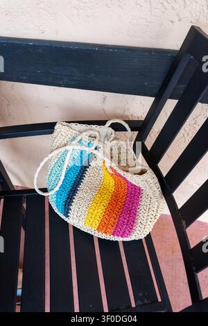 Bunte Strandtasche auf dem schwarzen Stuhl platziert, vertikales Foto Stockfoto