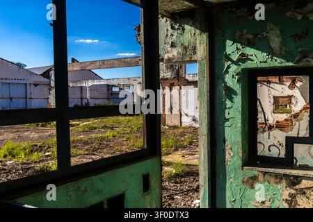 Innensicht eines verfallenen und zerfallenden Gebäudes mit abblätternder grüner Farbe an den Wänden. Ein Blick durch Betonfensterrahmen zeigt ein völlig verlass Stockfoto