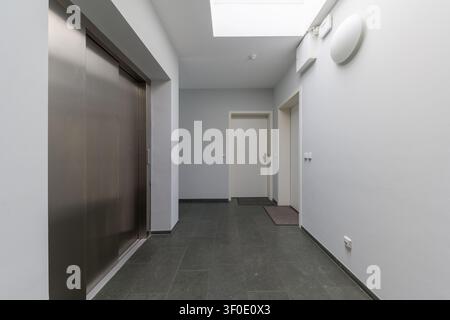 Innenarchitektur eines hellen und modernen Wohngebäudes mit schlanken Aufzugstüren aus Edelstahl, weißen Eingangstüren für Wohnungen, Stockfoto