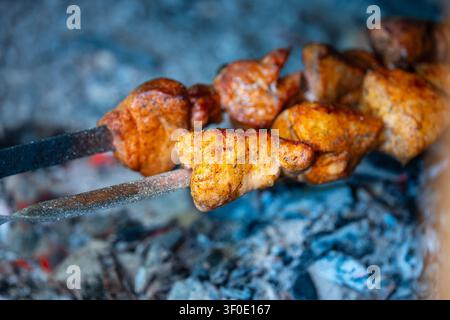 Nahaufnahme von saftigen Fleischstücken auf Metallspießen, die auf einem Außengrill mit Glut garen Stockfoto