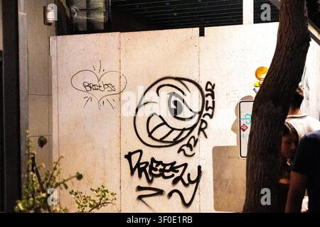 Städtische Mauer mit Graffiti bei Nacht mit Baum und vorbeigehenden Fußgängern Stockfoto