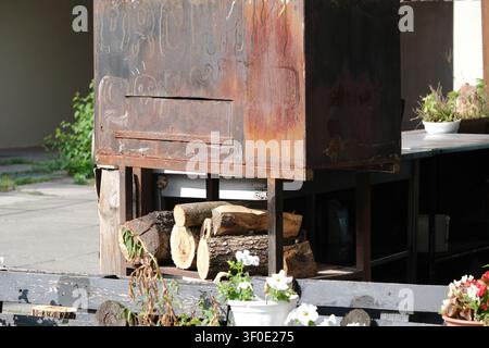 Rustischer Holzgrill im Freien mit gestapeltem Brennholz bei natürlichem Tageslicht, der traditionelle Grillgeräte und authentische Außengastronomie-Ausrüstung präsentiert Stockfoto