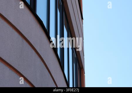 Minimalistische Ansicht einer modernen Gebäudefassade mit reflektierenden Glasfenstern, klaren architektonischen Linien und blauem Himmelsfreiraum. Stockfoto
