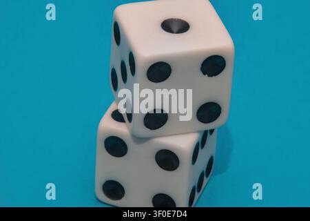 Nahaufnahme im Studio zeigt zwei klassische weiße Casinowürfel, die vertikal gestapelt sind und schwarze Punkte haben. Die Würfel sind deutlich gegen einen lebendigen blauen Bac sichtbar Stockfoto