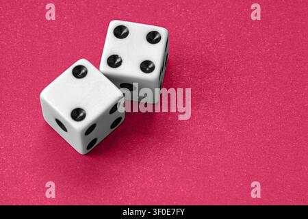 Paar weiße Würfel mit schwarzen Punkten auf einem hellroten, strukturierten Hintergrund. Stellten Glück, Zufall, Glücksspiel, Wahrscheinlichkeit und Entscheidungsfindung beim Glücksspiel dar Stockfoto