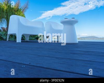 Freiluftszene mit zwei Stühlen und einem kleinen Tisch auf einer Terrasse mit Grünpflanzen und Himmelshintergrund an einem sonnigen Tag. Stockfoto