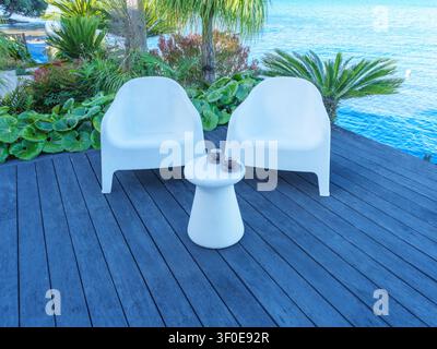 Außeneinrichtung mit zwei Stühlen und einem kleinen Tisch auf einer Terrasse mit grüner Kulisse an einem sonnigen Tag. Stockfoto